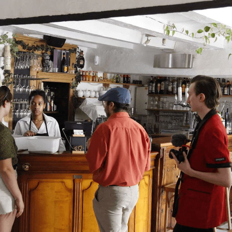 client discutant avec serveuse au comptoir d'un bar pendant qu'un cameraman filme